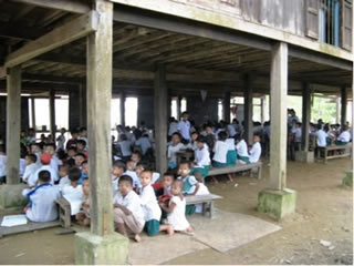 高床式に設計された僧院の床下が臨時の校舎。椅子や机が足りず、地面にゴザを敷いただけの場所で授業を受ける子どもたち