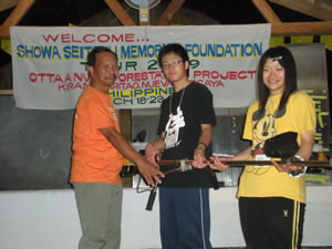 贈呈式では芦北高校の生徒（右、中央）から、プロジェクト 責任者のロペス氏（左）へ草刈機が手渡されました 