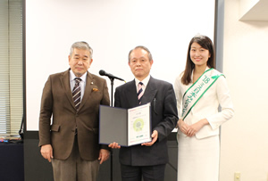任命書は、UNDB-J委員長代理の涌井史郎氏（左）より廣 瀬道男副理事長に授与。写真右は、グリーンウェイブ大使 に任命された「2018ミス日本みどりの女神」の竹川智世氏 